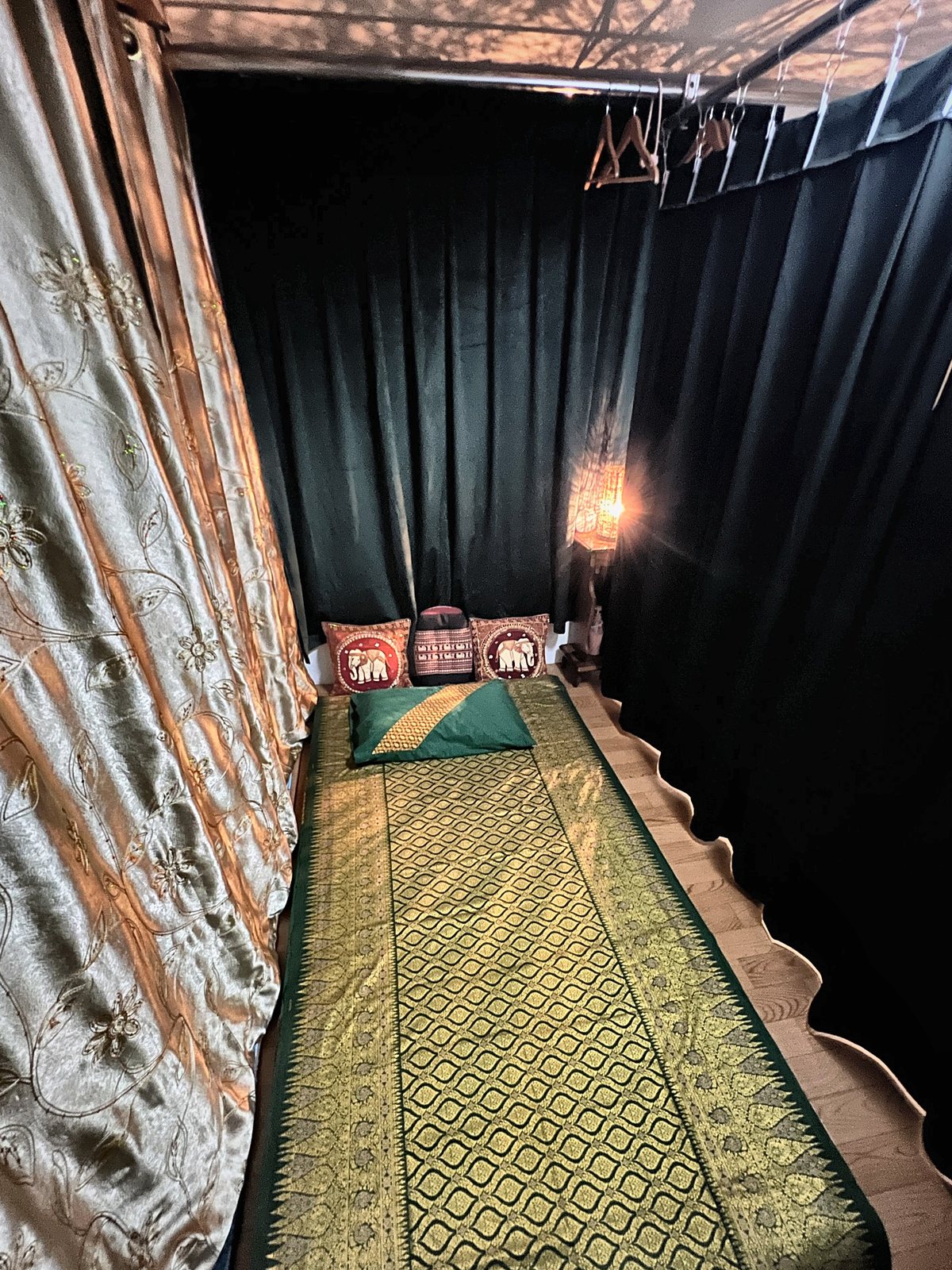 Thai massage mat with gold-and-green silk cover in a private curtained space